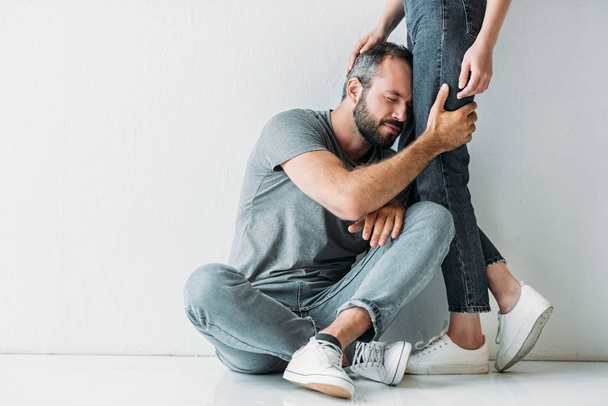 cropped shot of upset man hugging legs of young woman - Photo, Image