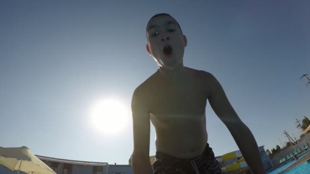 Small boy is jumping in the swimming pool outdoors at sunset in slow motion                                   A cheerful view of a sportive boy jumping in the paddling pool with celeste waters outdoors at a splendid sunset with splashes in slo-mo - Video, Çekim