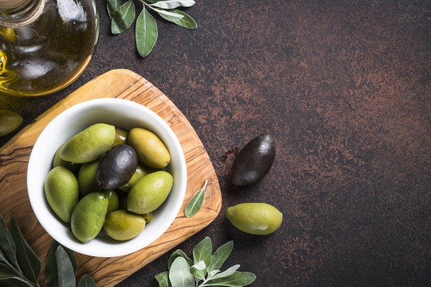 Black and green olives in a bowl and olive oil bottle on dark stone table. Top view with copy space. - Photo, Image