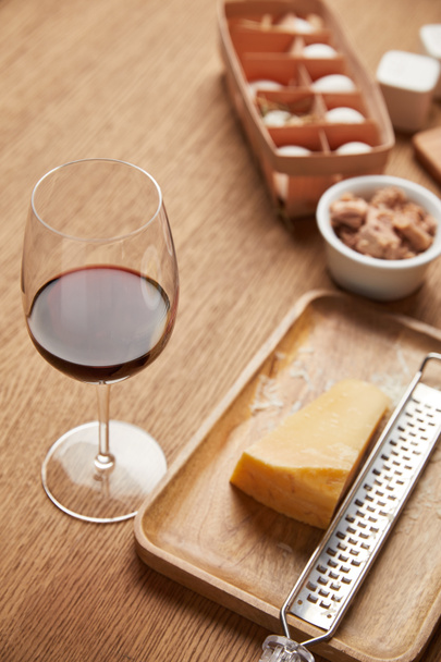 Nahaufnahme von geriebenem Käse und einem Glas Rotwein auf einem Holztisch - Foto, Bild