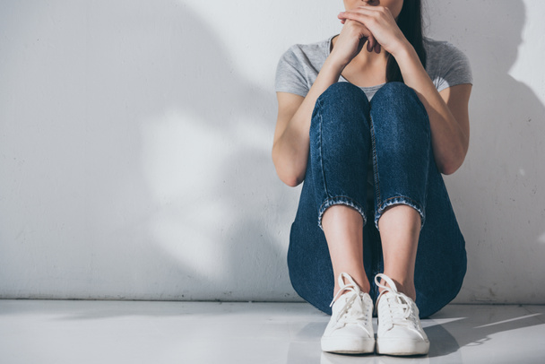 Oříznout záběr depresi mladá žena sedící na podlaze šedá stěna - Fotografie, Obrázek