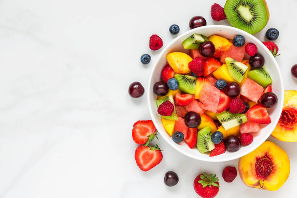 Миска здорового свіжого фруктового салату на білому мармуровому фоні. здорова їжа. вид зверху з простором для копіювання
 - Фото, зображення