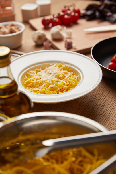 close-up shot of plate on spaghetti surrounded with ingredients on wooden table - Foto, Imagem