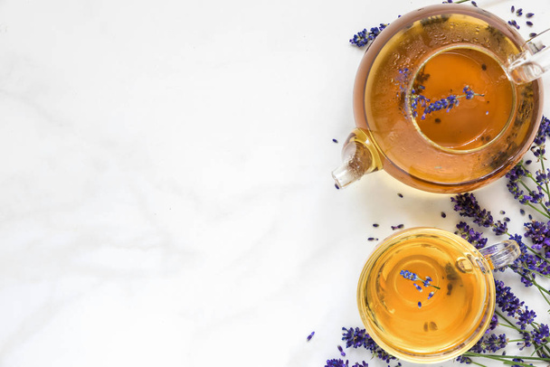 lavendel thee in een kopje en theepot met verse bloemen over witte marmeren tafel. kruiden drankje. bovenaanzicht met kopie ruimte - Foto, afbeelding
