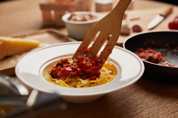 close-up shot of wooden spatula putting sauce onto pasta on wooden table - Valokuva, kuva