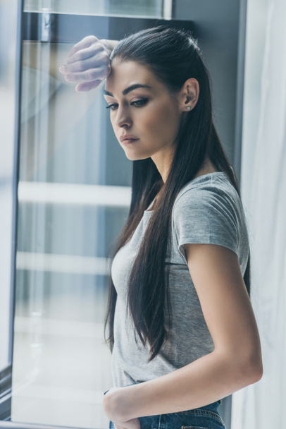 depressive young brunette woman leaning at window and looking away - Foto, Imagem