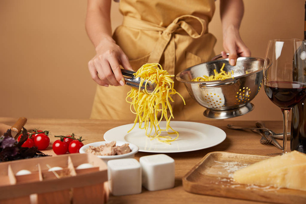 rajattu kuva nainen esiliina laittaa spagettia lautaselle siivilästä
 - Valokuva, kuva