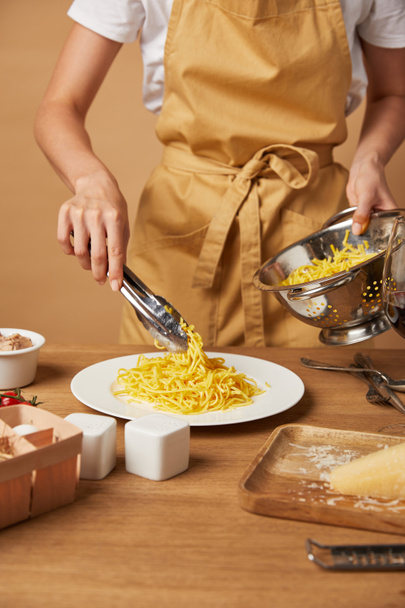 tiro recortado de mujer en delantal poniendo espaguetis en el plato con pinzas de colador
 - Foto, imagen