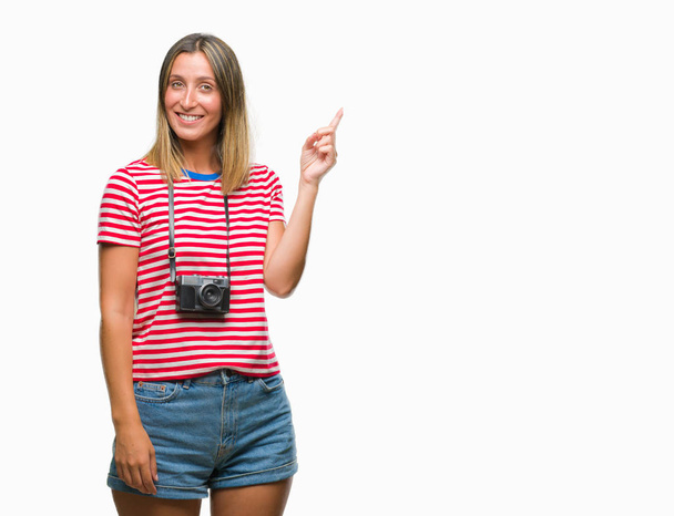 Mladá krásná žena pořizování snímků s použitím ročník fotografické kamery nad izolované pozadí s velkým úsměvem na tváři, rukou a prstu přejdete na straně při pohledu na fotoaparát. - Fotografie, Obrázek