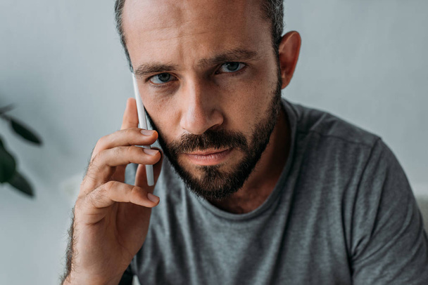 upset bearded man talking by smartphone and looking at camera  - Foto, Bild