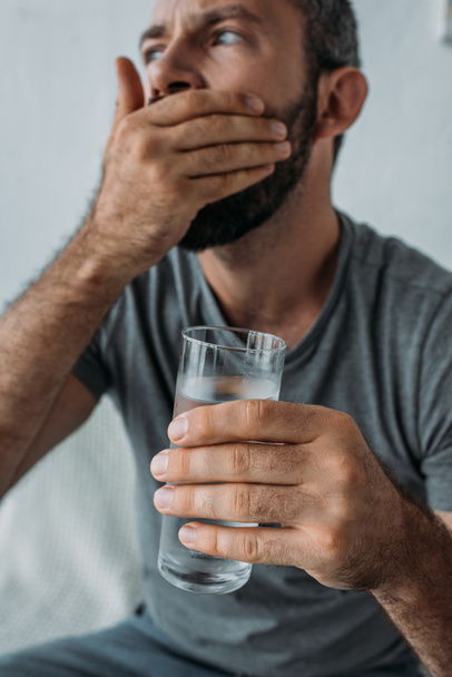 close-up view of bearded mid adult man holding glass of water and taking medicine - Foto, imagen