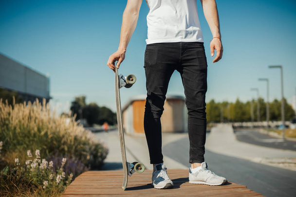 Close up of young man holding longboard or skateboard in the park. - Photo, Image
