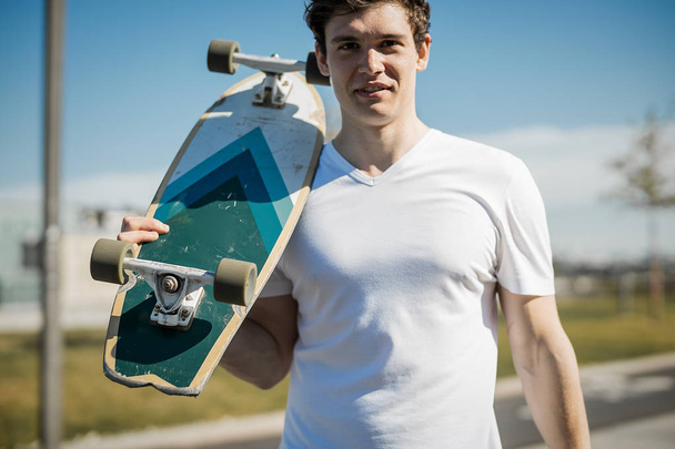 Young man in white T-shirt holding longboard or skateboard in the skatepark. - Fotoğraf, Görsel
