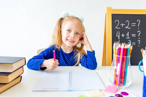 Happy cute industrious child is sitting at a desk indoors - Foto, Imagen