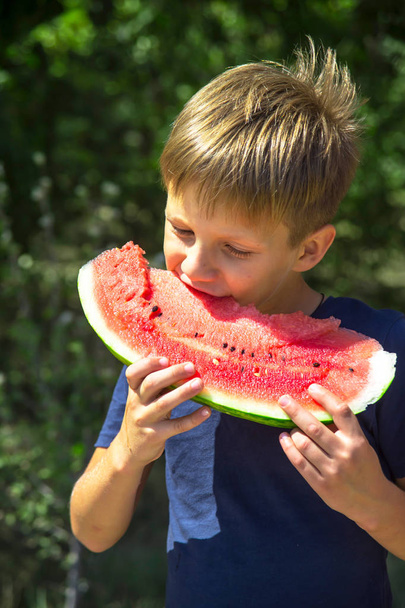 Kaukázusi fiú gazdaság és fog egy harap, nagy darab vörös érett görögdinnye. Nyári és őszi szezon. Egészséges nyers élelmiszerek, és vitaminok koncepció - Fotó, kép