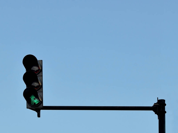 Green traffic light installed on a pole above a roadway, against a blue sky, copy space - 写真・画像