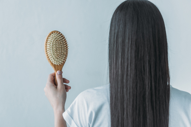 arkadan görünüşü düşmüş saçları gri izole saç fırçası tutan esmer kadın - Fotoğraf, Görsel
