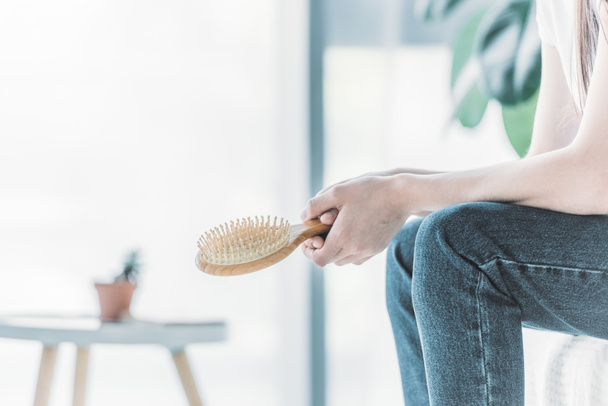 cropped shot of young woman holding hairbrush while sitting indoors, hair loss concept - Photo, Image