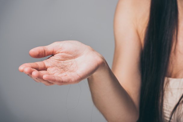 tiro recortado de mujer joven sosteniendo el pelo caído en la mano aislado en gris, concepto de pérdida de cabello
 - Foto, Imagen