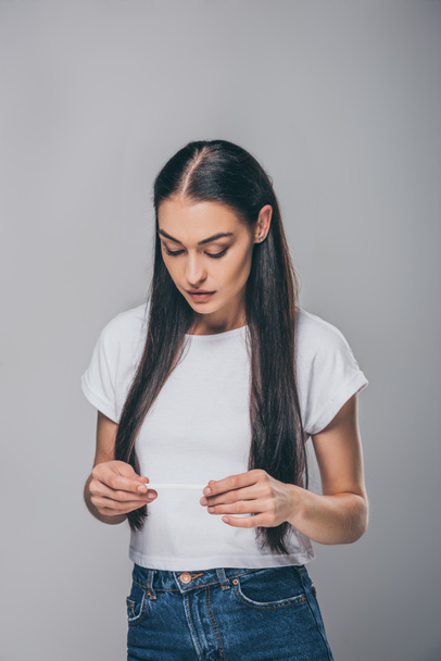 frustrated young woman holding pregnancy test isolated on grey   - Fotografie, Obrázek