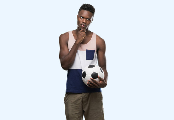 Jeune homme afro-américain tenant ballon de football visage sérieux réfléchissant à la question, idée très confuse
 - Photo, image