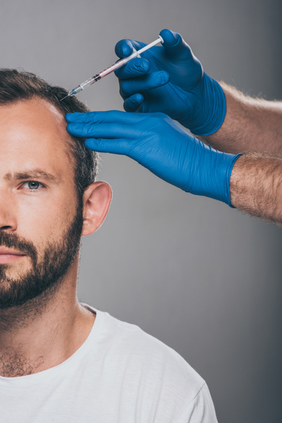 inyección recortada de médico con jeringa inyectable al hombre con alopecia mirando a la cámara aislada en gris
  - Foto, imagen