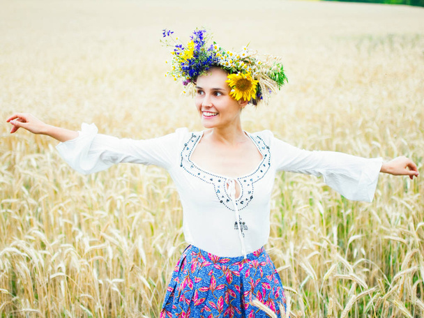 Ukrainian girl in a beautiful wreath walks through the summer meadow. The girl is dressed in ethnic clothes with embroidery. Feast of Ivan Kupala - Valokuva, kuva
