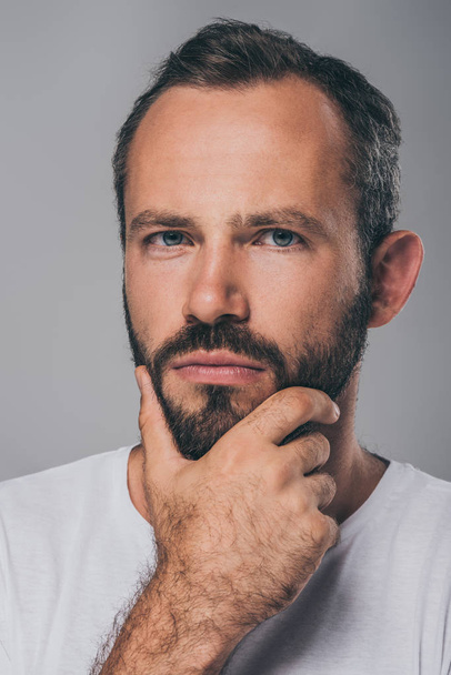 portrait of serious bearded man with hand on chin looking at camera isolated on grey  - Foto, Imagen