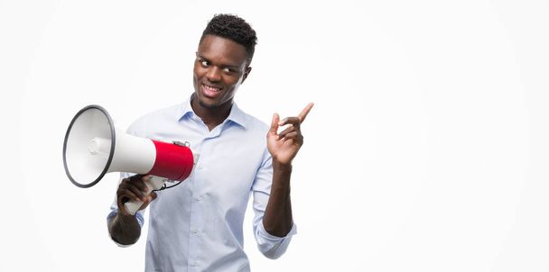 Jeune homme afro-américain tenant mégaphone très heureux pointant avec la main et le doigt sur le côté
 - Photo, image