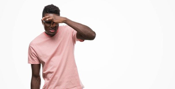 Jovem afro-americano vestindo camiseta rosa cheirando algo fedorento e nojento, cheiro intolerável, segurando a respiração com os dedos no nariz. Maus cheiros conceito
. - Foto, Imagem