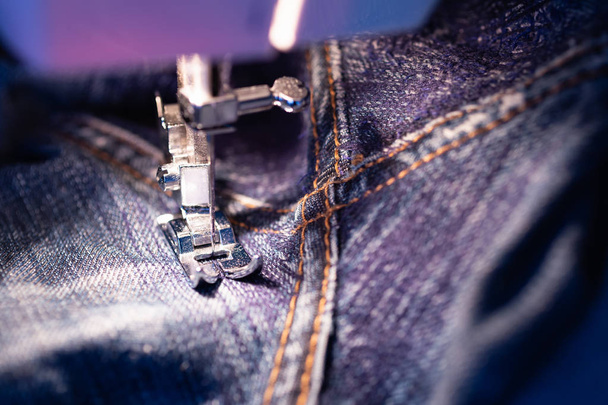 Reparação de jeans na máquina de costura. Vista do tecido, agulha e linha. Iluminação da lâmpada incandescente embutida. Jeans são um tipo de calças, tipicamente feitas de ganga ou pano de calça
 - Foto, Imagem