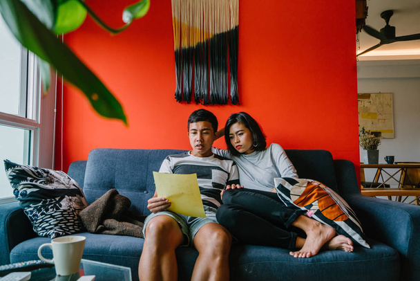 Malay couple as they sit on a couch and read together. They are young, attractive and relaxed as they enjoy the weekend together on their couch in their living room. - Fotó, kép