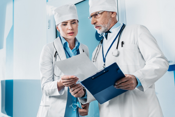 серьезные врачи мужского и женского пола смотрят на бумагу и обсуждают ее в больничном коридоре
  - Фото, изображение
