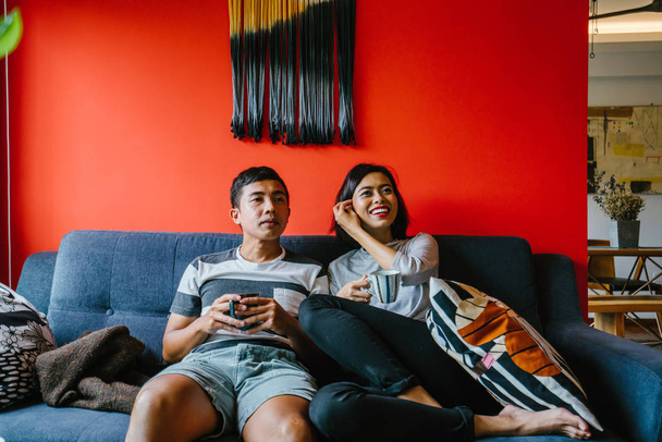 Malaiisches Ehepaar sitzt gemeinsam auf der Couch in einem trendigen und modernen Wohnzimmer - Foto, Bild