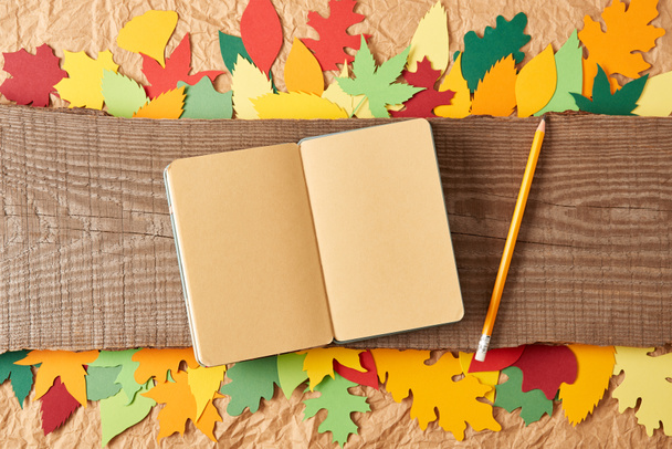 tendido plano con cuaderno en blanco, lápiz en tablón de madera y hojas de papel artesanal de colores sobre fondo de papel arrugado
 - Foto, Imagen