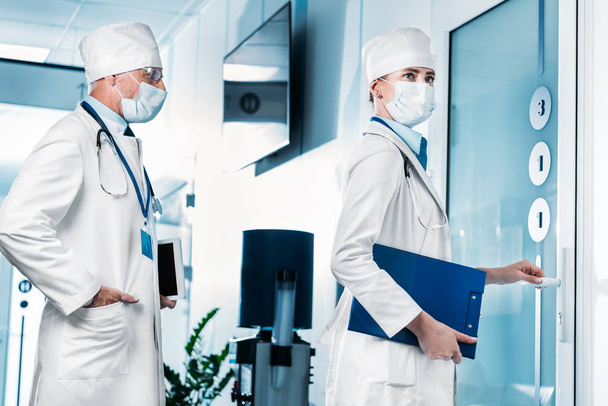 doctora con portapapeles abriendo la puerta mientras su colega espera en el pasillo del hospital
  - Foto, imagen