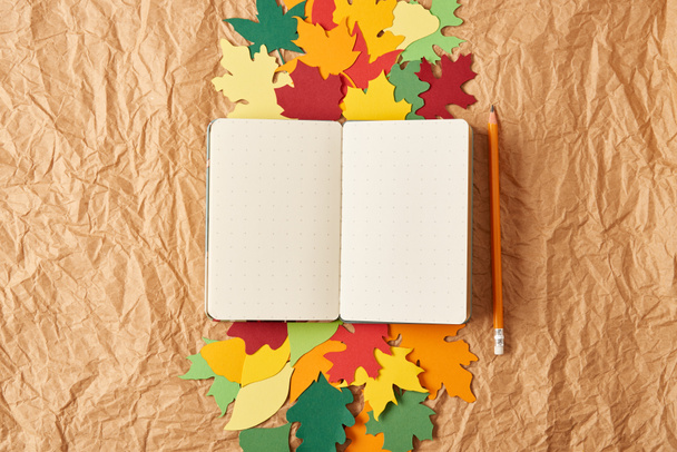 flat lay with blank notebook, pencil and colorful handcrafted paper leaves on crumpled paper background - Φωτογραφία, εικόνα