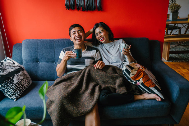 married Malay couple sit on their couch in a trendy and modern living room together - Фото, зображення