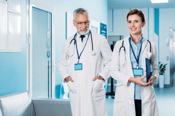 felici medici di sesso femminile e maschile con distintivi e stetoscopi sul collo passeggiando nel corridoio ospedaliero
  - Foto, immagini