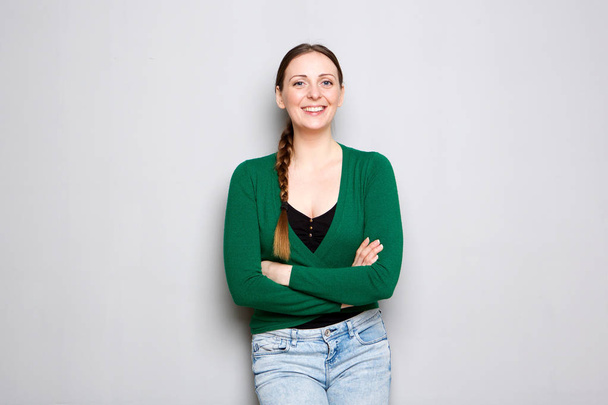 Портрет счастливой молодой женщины, стоящей у серой стены со скрещенными руками
 - Фото, изображение