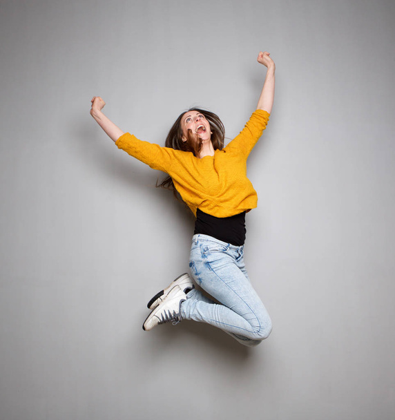 Action-Porträt einer jungen Frau, die vor grauem Hintergrund in die Luft springt - Foto, Bild