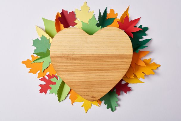 top view of wooden heart shaped board and colorful handcrafted leaves on white surface - Φωτογραφία, εικόνα