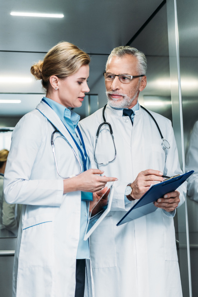 врач-мужчина показывает планшет коллеге-женщине с цифровым планшетом в лифте больницы
  - Фото, изображение