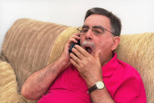 Ritratto di un uomo anziano che sbadiglia, che parla al telefono. conversazione noiosa
. - Foto, immagini