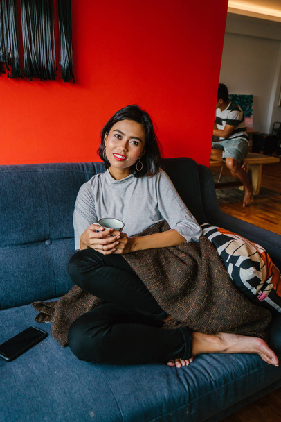 Portrait of a Singaporean Malay woman sitting on a comfortable blue couch  in a trendy living room during the daytime. She is relaxing and chilling out on her own on a weekend.  - Foto, Bild