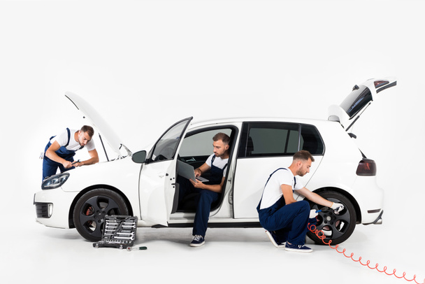 pneu inflável mecânico bonito do automóvel, usando o portátil e olhando no capuz no branco
 - Foto, Imagem