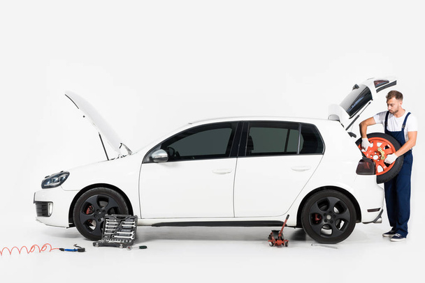 mécanicien automobile prenant pneu du coffre de la voiture sur blanc
 - Photo, image