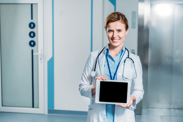 vrouwelijke arts lachend met de stethoscoop over hals digitale tablet met leeg scherm tonen in ziekenhuis  - Foto, afbeelding
