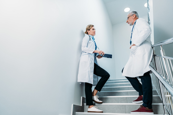 side view of male and female doctors talking on staircase in hospital  - Photo, Image