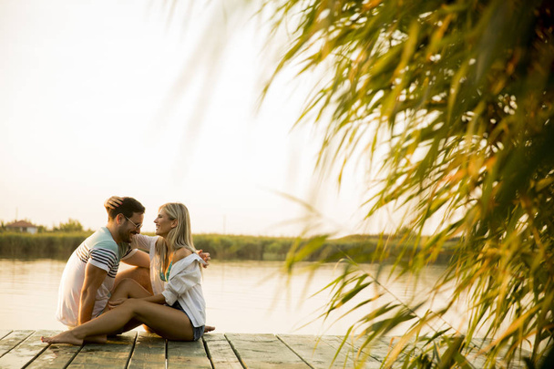 Casal romântico sentado no cais de madeira no lago no dia ensolarado
 - Foto, Imagem
